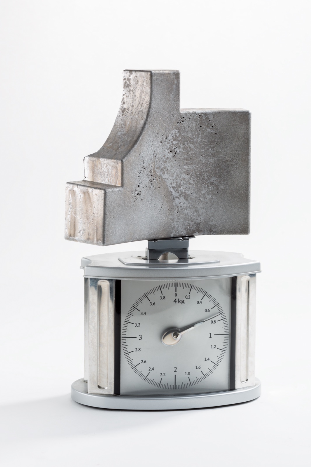 Ein großes Formteil aus Aluminiumschaum steht auf einer mechanischen Haushaltswaage; der Zeiger steht deutlich unter einem Kilogramm.