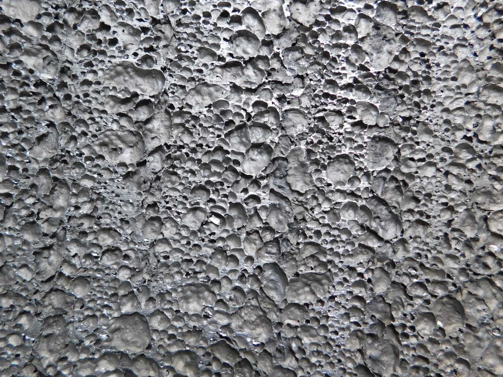 Formatfüllende Nahaufnahme einer Aluminiumschaum-Schnittfläche: dicht an dicht liegende, unterschiedlich große Poren mit metallisch glänzenden Stegen dazwischen.