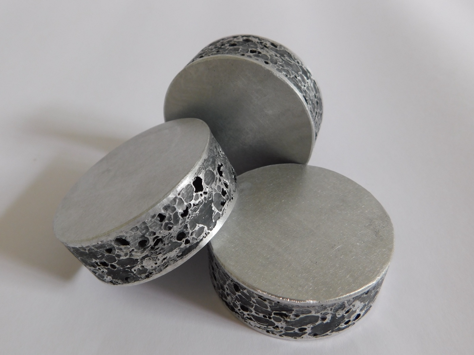 Drei runde Aluminiumschaum-Ronden übereinander gelegt; die Deckflächen sind glatt überfräst, an den Mantelflächen liegt die Porenstruktur offen.