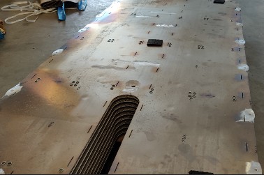 Große flache Bodenplatte auf dem Hallenboden, mit zahlreichen Bohrungen und einem Bündel dünner Rohre an der Stirnseite.