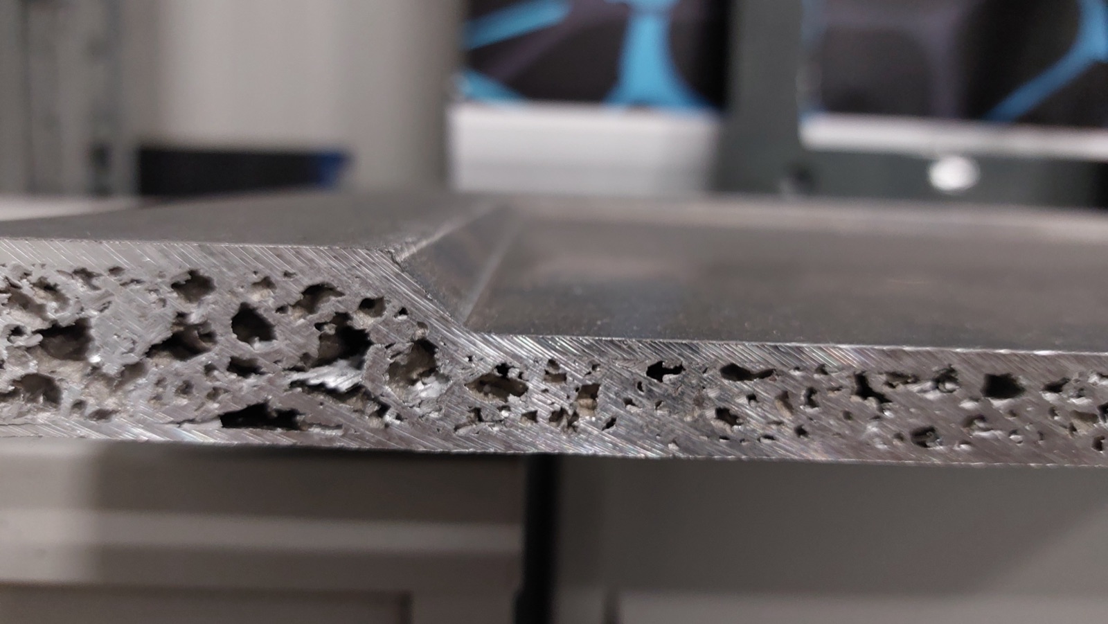 Nahaufnahme der Kante einer Bodenplatte: Der Aluminiumschaumkern liegt an der bearbeiteten Schnittfläche offen, die Kante ist abgeschrägt und läuft zu einer dünneren Randzone aus.