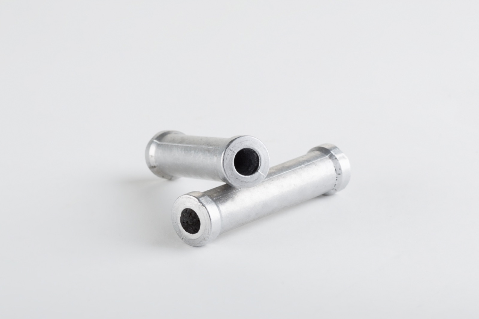 Zwei kleine zylindrische Bauteile aus Aluminium; an den offenen Stirnseiten ist der dunkle Aluminiumschaumkern zu sehen.