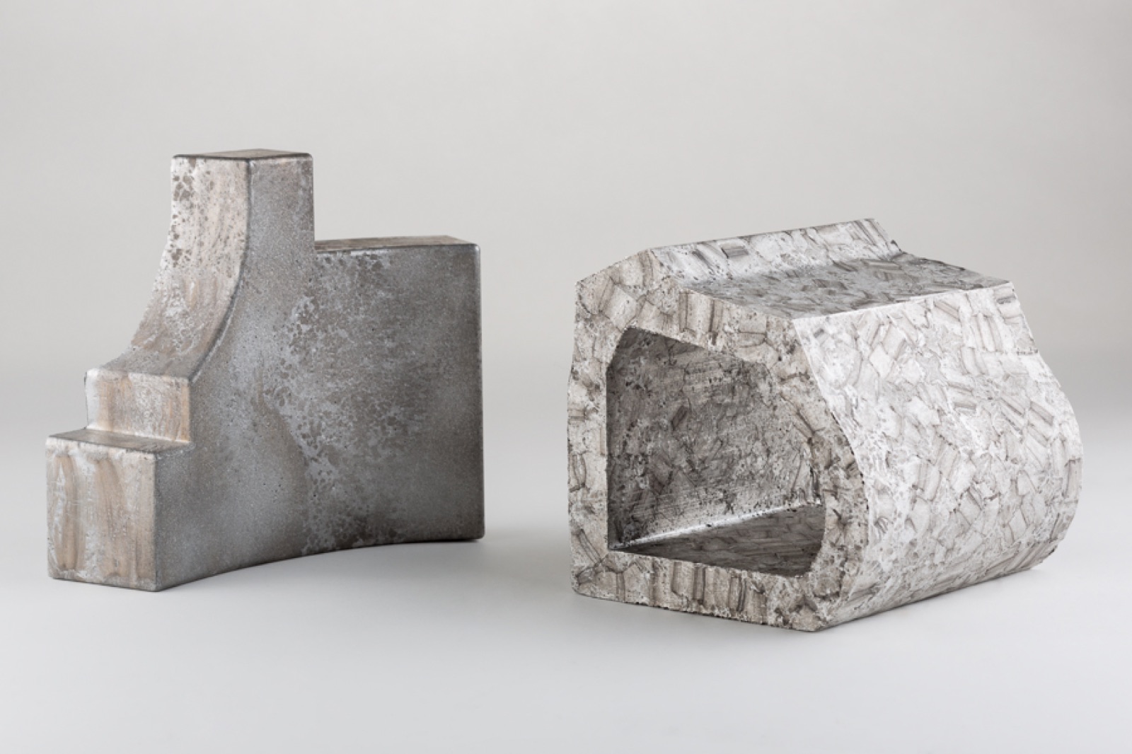 Zwei Formteile aus Aluminiumschaum nebeneinander: links ein gestuftes Bauteil mit geschlossener, glatter Gusshaut, rechts ein Teil mit rechteckigem Durchbruch und grob strukturierter Oberfläche.
