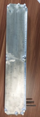 Schmale, metallisch blanke Platte mit verschraubten Anschlüssen an beiden Schmalseiten, daneben zwei dünne Rohre.