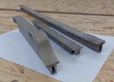 Drei in Form geschäumte Aluminiumschaum-Profile unterschiedlicher Länge, nebeneinander auf einem hellen Bogen.