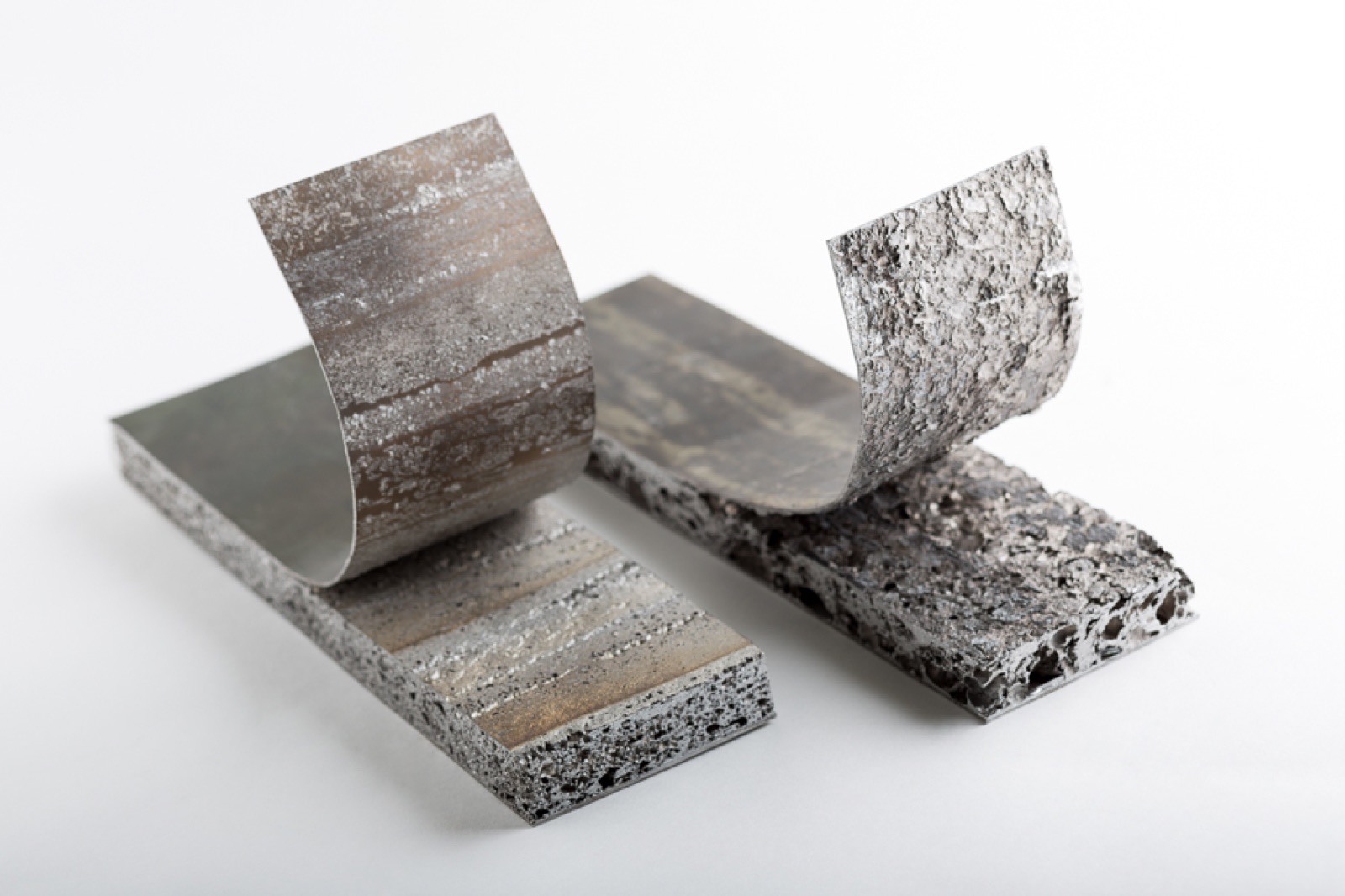 Zwei Sandwichproben, bei denen die Decklage zurückgebogen wurde. An den Unterseiten der zurückgebogenen Decklagen haftet weiterhin Aluminiumschaum.