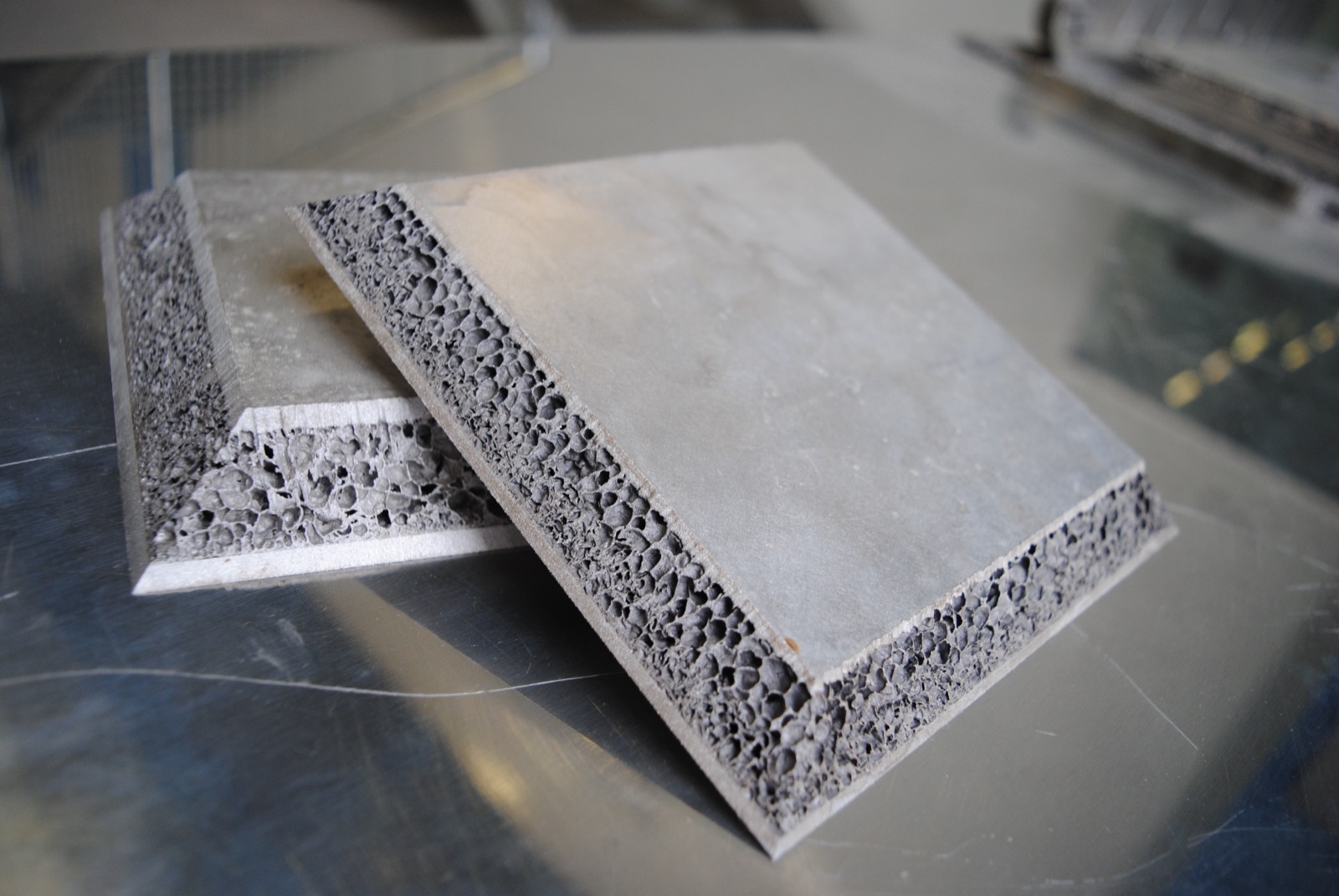 Zwei Sandwichplatten übereinander auf einem Werkbanktisch, beide mit angefasten Kanten; an den Fasen liegt der Aluminiumschaumkern zwischen den Decklagen offen.